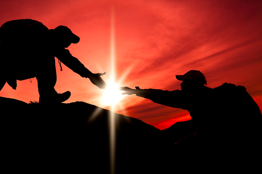 One person helping another person climb a mountain